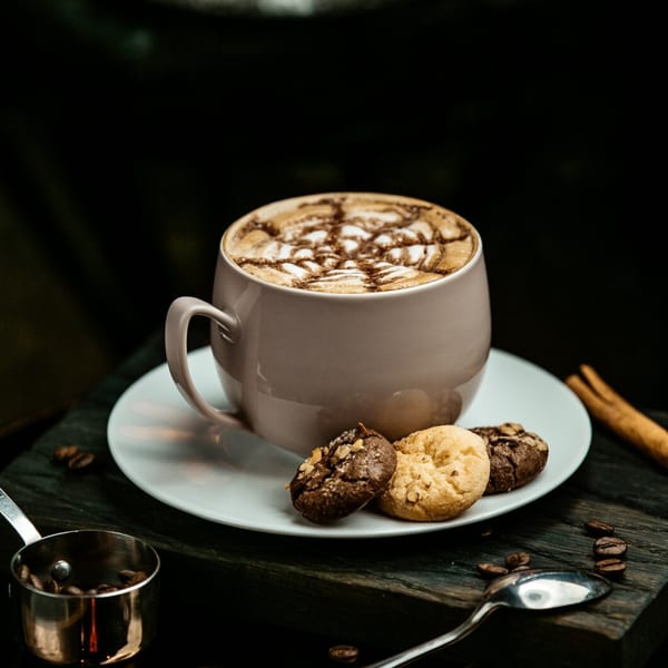 A Java House latte with intricate foam art, served with two cookies on a white saucer.