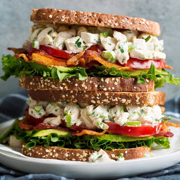 A towering Java House chicken salad sandwich with bacon, lettuce, tomato, and avocado on whole grain bread.