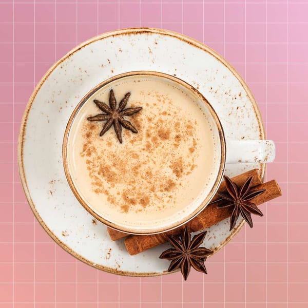 Overhead view of a Java House chai latte with star anise and cinnamon sticks on a pink grid background.